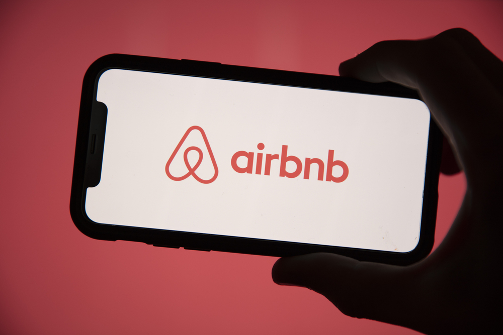 Main tenant un smartphone sur lequel le logo d’Airbnb est affiché